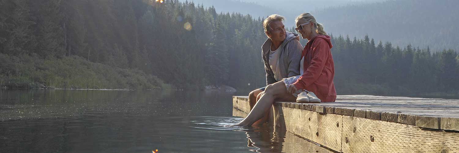 Middle aged couple sitting on a wooden dock over looking a picturesque lake and forrest.